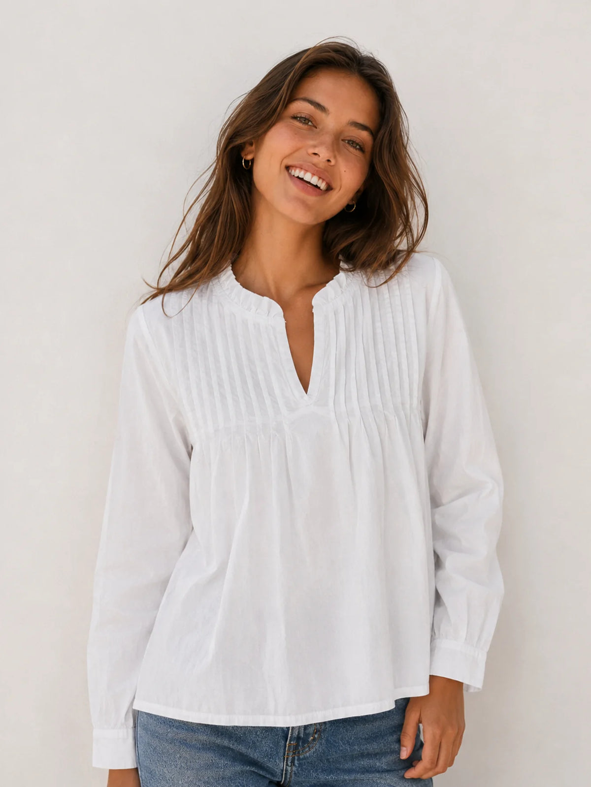 Detalle de pliegues verticales en la parte delantera de la blusa blanca de algodón