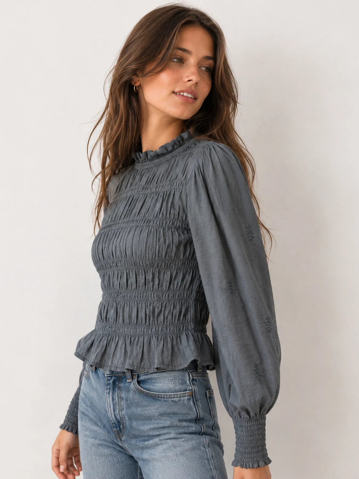 Vista lateral de blusa fluida de manga larga con cuello subido y acabado de nido de abeja