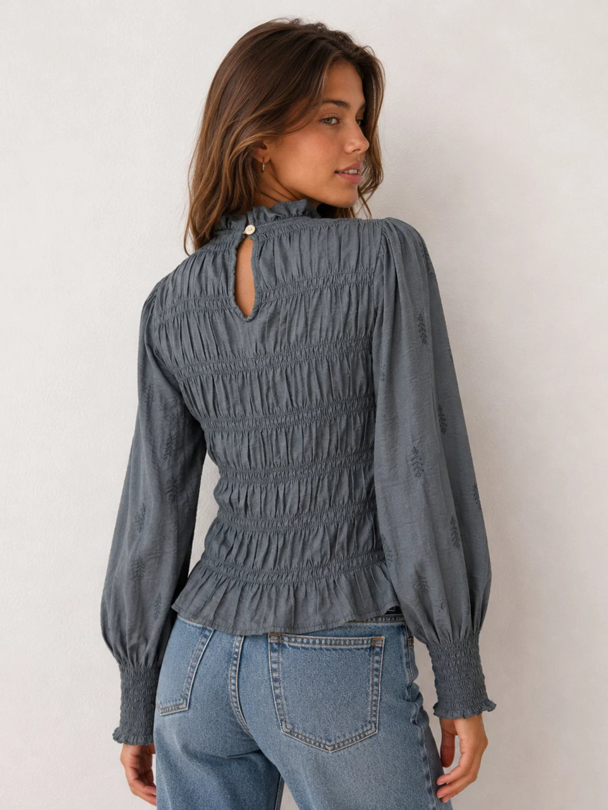 Detalle del cuerpo elástico con nido de abeja y bordados en la blusa gris