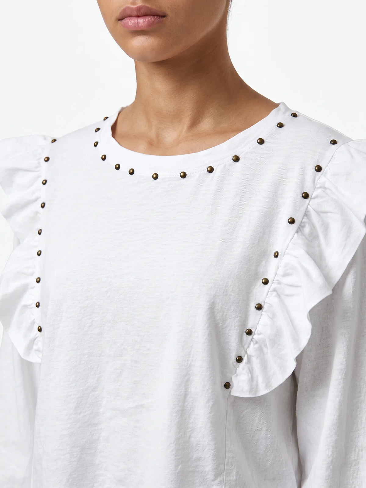 Detalle del cuello redondo con tachuelas metálicas y volantes en camiseta blanca